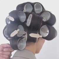 Close-up of SOPHIA MAE Creaseless Hair Clips securing sections of dark hair around large rollers during styling.